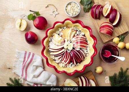 Food, Women's hands hold a jar of jam. The process of making an apple cake or pie on a wooden table. Apple pie with cranberry jam and baking ingredien Stock Photo