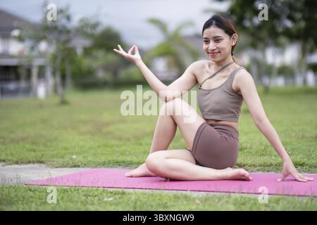 A young woman practicing a seated yoga pose on a mat outdoors, promoting relaxation and mindfulness Stock Photo