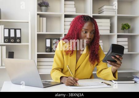 Accountant young african businesswoman using calculator for document accounting financial sitting at computer in workplace office on laptop Stock Photo