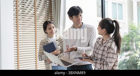 Three students engaged in a lively discussion, sharing ideas and working together in a bright, modern study environment Stock Photo