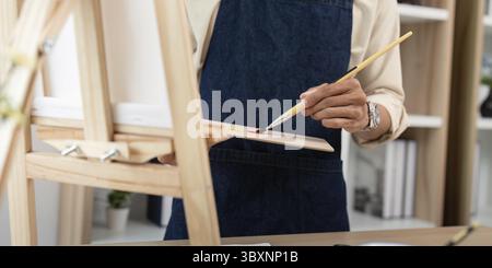 Close-up of an artist's hands holding a brush and palette, painting in a studio. Focus on the creative process and tools Stock Photo