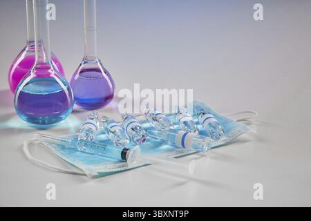 Three medical flasks with purple and pink chemical reagents. Seven mockup ampoules with liquid, syringe and mask isolated on white. Laboratory researc Stock Photo