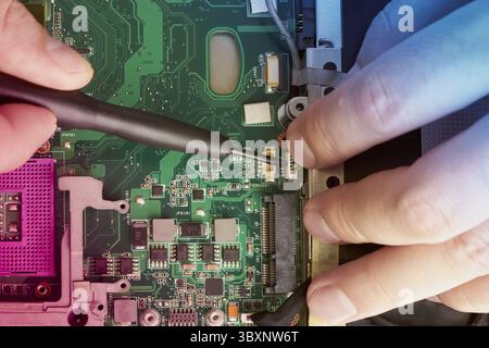 Man repairs computer. A service engineer in a shirt repairs a laptop, at a white Desk against a white wall. Computer motherboard background with blur Stock Photo