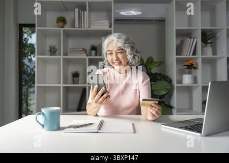 An elderly woman enjoys online shopping using her credit card showcasing the blend of technology and lifestyle Stock Photo