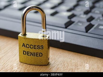 Access Denied text engraved on padlock with keyboard background. Password and use access concept Stock Photo