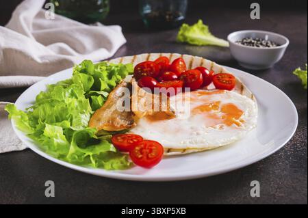 Food, Appetizing tacos with fried egg, bacon, tomato and lettuce on a plate on the table Stock Photo