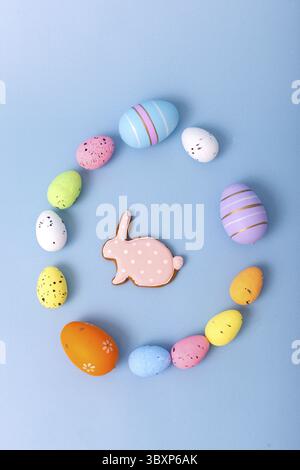 Beautiful decorative multicolored eggs and pink gingerbread in the form of a rabbit are scattered on a light blue background in an egg-shaped frame, t Stock Photo