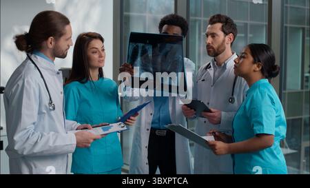 Group of five multiethnic medical students interns men women doctors analyzing patient x-ray result using digital tablet writing clipboard consulting Stock Photo