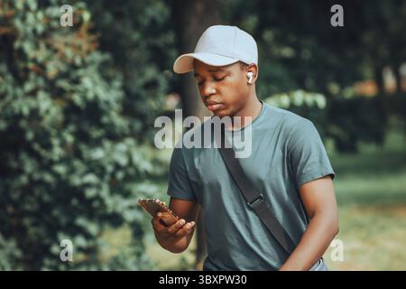 a dark-skinned guy walks through the park and holds a phone in his hand Stock Photo