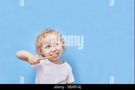 Child brushes his teeth with a wooden bamboo toothbrush on a blue background with a copy space Stock Photo