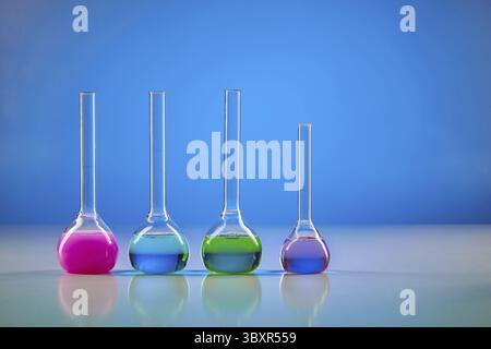 Four medical flasks with colorful chemical reagents for tests, blue background. Laboratory research of Coronavirus. Worldwide pandemic COVID-19, 2019- Stock Photo