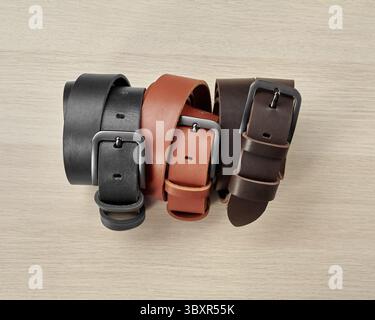 Three folded leather belts of different colors with stylish buckles and DAD embossing on loop arranged on light wooden background. Stylish personalize Stock Photo
