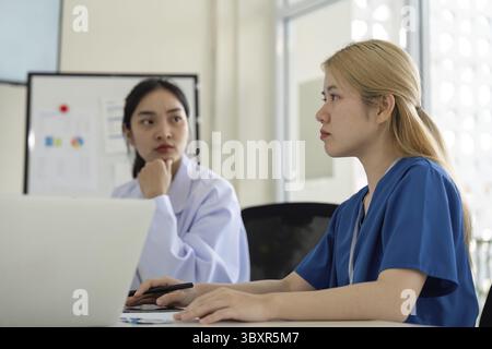 Two diverse female healthcare professionals actively engaged in a focused discussion, collaborating on strategies for patient care during a team meeti Stock Photo