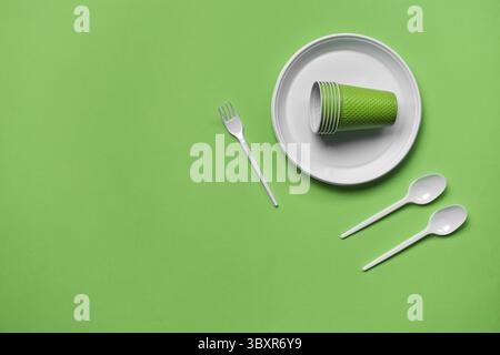 Colorful plastic disposable tableware, such as plate, two spoons, fork, folded cups on green background with copy space. The concept of picnic utensil Stock Photo