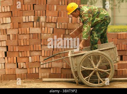 June 22, 2006, BEIJING, CHINA: A Chinese worker fills a wheelbarrow full of bricks next to a construction site in central Beijing, China on June 22, 2006  Beijing, like many of China's major cities, is a vibrant tale of two cities;  a city aggressively pushing towards a future, high-tech megalopolis but still very much a city chained to much of its low-tech past. (Credit Image: © Stephen Shaver/ZUMA Press Wire) Stock Photo