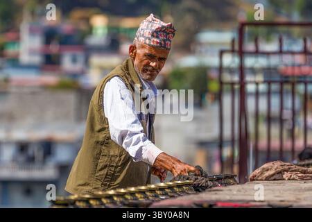 An older Nepali Hindu man in a Dhaka topi cap cleans butter lamps at ...