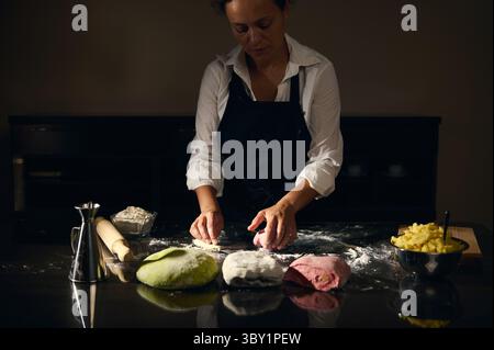 A woman chef kneads colorful pasta dough representing the Italian flag in a cozy kitchen, focusing on traditional Italian culinary artistry. Perfect f Stock Photo