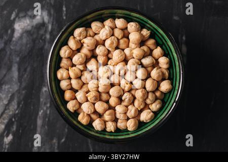 Chickpeas in green bowl. Dry legumes on dark marble background. Plant-based protein ingredient. Natural vegan food close-up. Rustic kitchen texture. Stock Photo