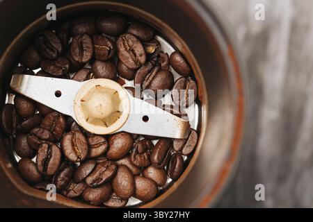 Coffee grinder with beans. Close-up of roasted coffee inside metal electric grinder. Sharp blade in center. Home brewing preparation. Stock Photo