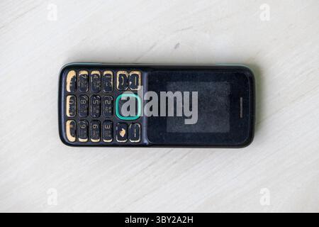 Aged feature phone, discolored body, and scratched screen from extensive use. Top-down view of a well-worn old button mobile for your projects. Stock Photo