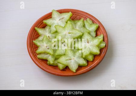 Freshly sliced star fruit (Averrhoa carambola), known as Kamranga in Bengali, arranged beautifully on a rustic clay plate. Healthy, vibrant tropical f Stock Photo