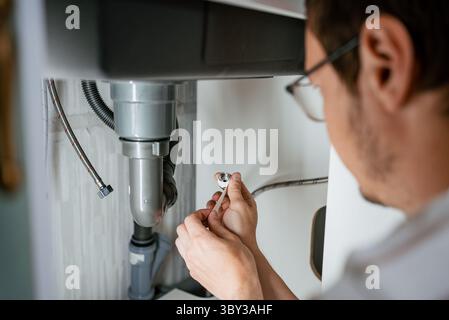 Professional plumber carefully wrapping teflon tape on pipe thread preparing to connect water pipe to mixer, ensuring secure and leak-free plumbing in kitchen sink Stock Photo