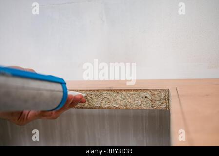 Worker uses a sealant gun to apply adhesive to the edge of a kitchen countertop, preparing for the installation of a new sink, ensuring a watertight and secure fit Stock Photo