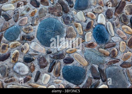 Stones of various shapes and colors are laid out on the road as a sidewalk close-up. Stock Photo