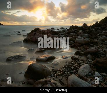 Waves of the Atlantic Ocean gently lap over rocks on the shoreline at sunset, near Mirleft in Sud Agadir,Morocco. Stock Photo