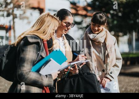 Three young women collaborating on notes outdoors in sunny weather Stock Photo