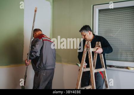 Two workers repainting a room with green walls during an indoor renovation project Stock Photo