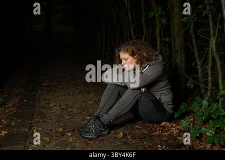 Woman sitting in dark forest, thoughtful and depressed, head resting on her arms Stock Photo