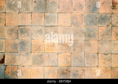 Orange brown white beige old shabby worn out floor tiles with damages cracks dirt caverns potholes and paint stains. Art design background texture Stock Photo