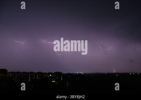 Horizontal lightning flashes across a purple night sky above a cityscape with apartment buildings. Distant bolt strikes the horizon. Long exposure cap Stock Photo