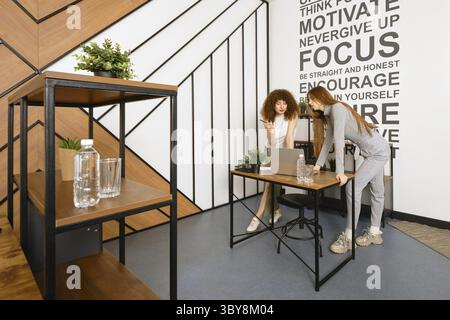 Two women are bent over a laptop and studying a prototype of their health monitoring program Stock Photo
