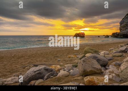 Coarse sand beach with stones. Colorful sunset over the calm sea Stock Photo