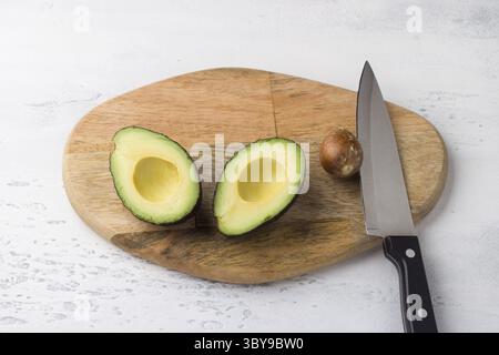 Food, Fresh avocado cut in half and avocado pit with a knife on a wooden board on a light gray background, top view Stock Photo