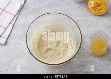 Food, Glass bowl with egg-butter mixture, freshly squeezed orange juice on a gray background. Cooking greek easter orange sesame koulourakia cookies s Stock Photo