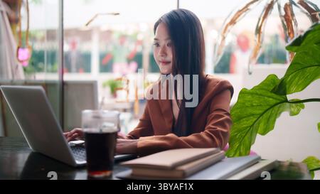 Modern Asian female professional engaging with technology in a contemporary setting. This image represents productivity innovation digital entrepreneu Stock Photo