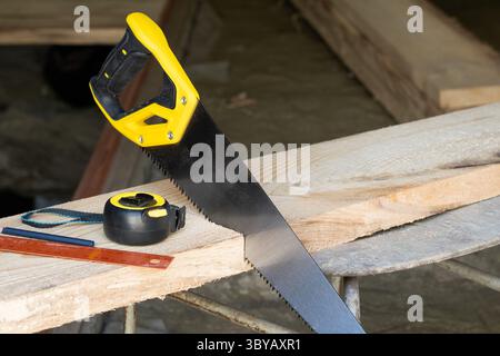 Hand saw, tape measure and a square on table in carpenters workshop. Carpentry tools Stock Photo