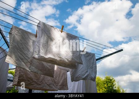 Laundry hanging on a rotary washing line against a bright blue sky with scattered clouds, capturing a fresh, breezy day and everyday domestic life. Stock Photo