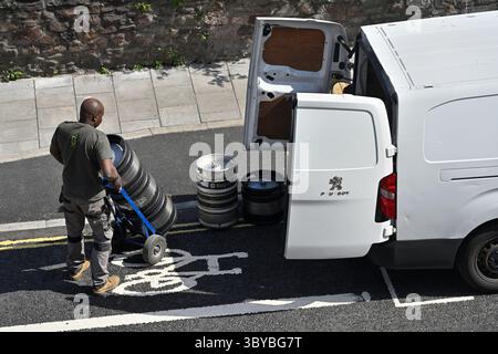 White van with man unloading heavy beer kegs from the rear while parked in a short loading bay by cycle lane on main road Stock Photo