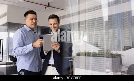 Two smiling men team members standing in office using tablet Stock Photo