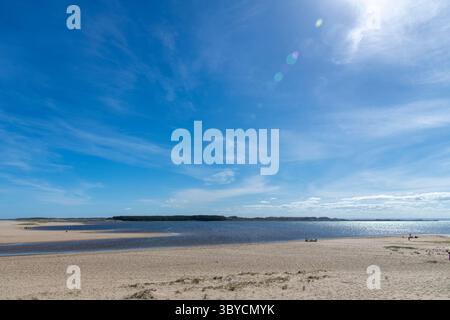 Panoramic view over water and beach of the lagoon Laguna de Rocha near La Paloma, Rocha, Uruguay with some people on the beach and sun shining bright Stock Photo