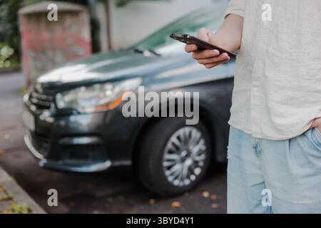 Hands of a young man using smart phone near the car outdoors. Concept of car remote control. Stock Photo