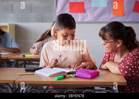 Elementary school female teacher helping one of her students during class inside a classroom. Stock Photo