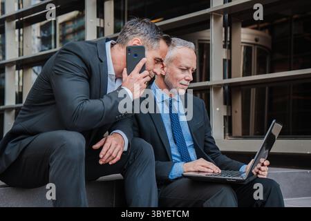 Two dedicated businessmen are intensely discussing important matters while reviewing information on a laptop. Their serious demeanor reflects Stock Photo