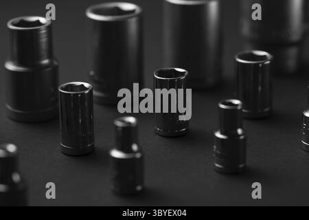 A dark, moody studio shot showcases a collection of black six-point sockets arranged on a black surface. The sockets vary in size Stock Photo