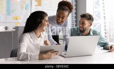 Three joyful workmates reviewing online task in office Stock Photo