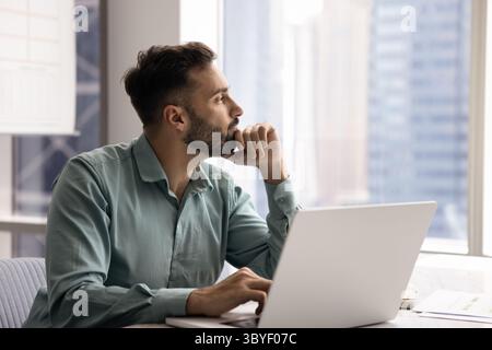 Pensive Latin man distracted from workflow looking out window Stock Photo